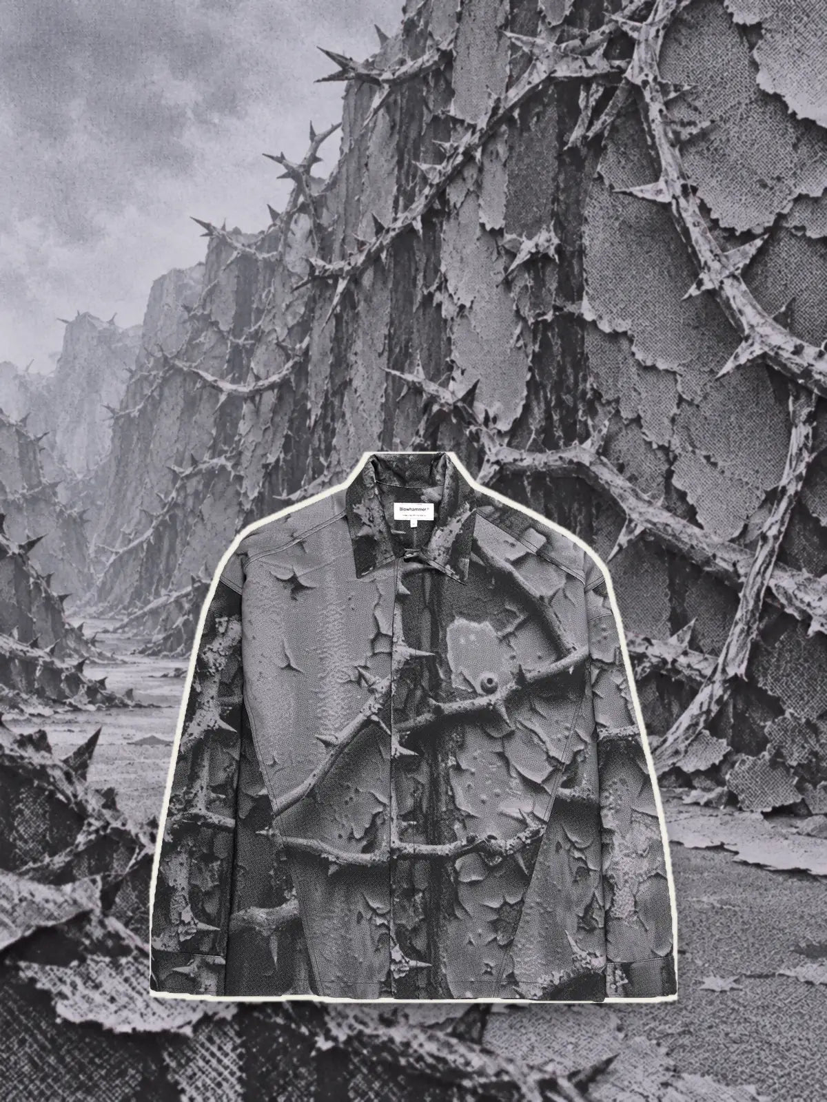La camicia a maniche lunghe grigia Bloodrose Dark, ritagliata con un bordo di carta chiara, davanti a un muro di rovi grigi in rilievo.