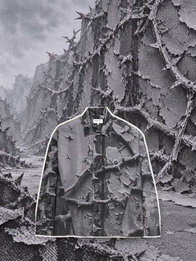 La camicia a maniche lunghe grigia Bloodrose Dark, ritagliata con un bordo di carta chiara, davanti a un muro di rovi grigi in rilievo.