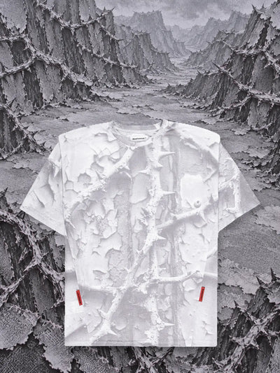 Den vita t-shirten Bloodrose White framför berg av törnsnår av grått papper i relief.
