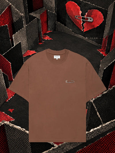 Den bruna t-shirten Brokenheart i ett rum av mörkt papper, under ett hjärta av rött papper, brutet i två delar.
