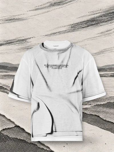 Den vita t-shirten Crux ovanför en korsning av stigar av vitt papper, med långa strimmor av grått kol som vinden bär.