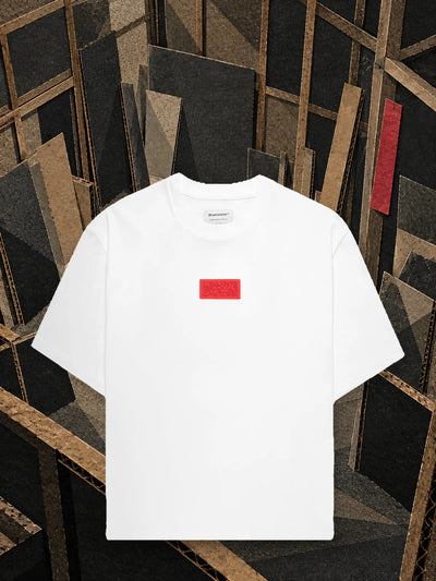 Den vita t-shirten Deconstructed i en halvfärdig verkstad av kartong, bland bjälkar och lutade paneler.