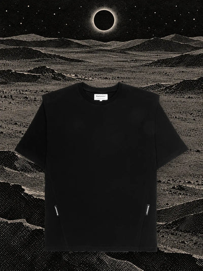 Den svarta t-shirten Eclipse på kullar av svart papper, under en förmörkelse med en ring av vitt ljus.