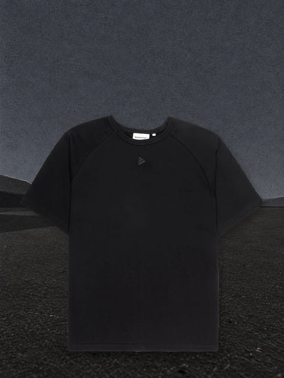 Den svarta raglan t-shirten Minimal på en slätt av svart papper, med dimma av ljust papper vid horisonten.