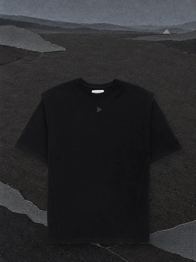 Den svarta t-shirten Minimal SP på en nästan tom slätt av svart papper, under en mörkgrå himmel av papper.