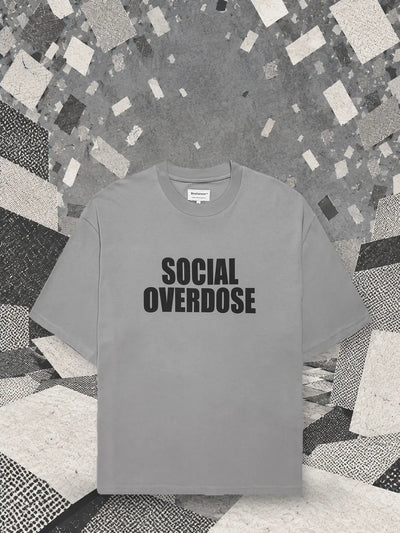 Den grå t-shirten Social Overdose under ett snöfall av små vita och grå kort, över ett landskap av pappersblock.
