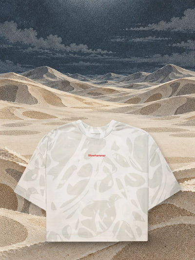 Den korta elfenbensfärgade t-shirten Strand Ivory ovanför dyner av elfenbens- och sandfärgat papper.