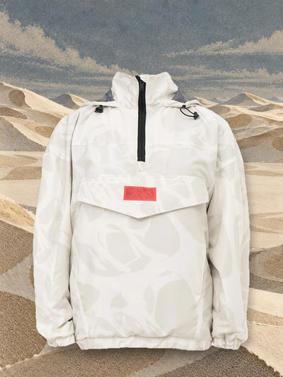 Den elfenbensfärgade anoraken Strand Ivory bland sandfärgade dyner av papper, under en himmel av ljust papper.