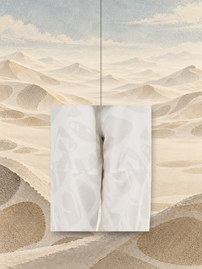 قطعة من طبعة سروال الجوغر العاجي Strand Ivory، معلّقة بخيط فوق كثبان من الورق بلون الرمل.