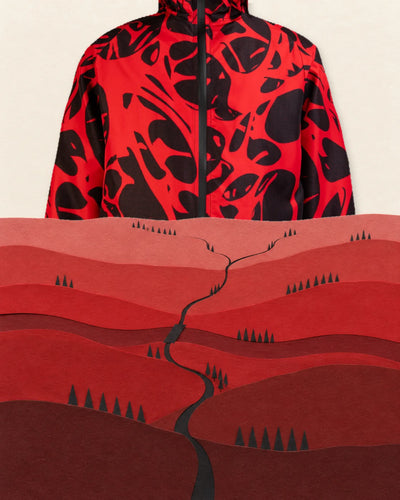 La giacca a vento Strand Red, enorme, esce come una montagna da dietro l'orizzonte di una valle di carta rossa, e il bordo in alto le taglia il collo. Le colline, in più file, ne coprono la parte bassa. Nella valle, piccolissimi, un sentiero nero che si divide, un ponte di carta su un fiume rosso scuro e file di alberi neri a cono.