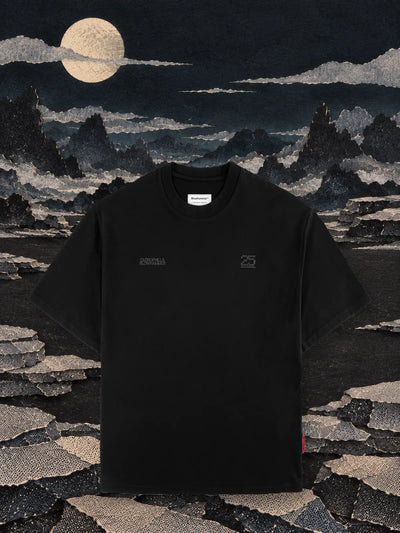 Den svarta t-shirten Vertebrae på en slätt av svart papper om natten, bland rader av staplade stenar av grått papper och månen.