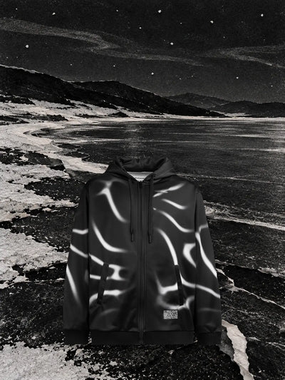 La felpa con cappuccio e zip nera Tidegrey su un lago nero ghiacciato di notte, con riflessi bianchi come le linee della stampa.