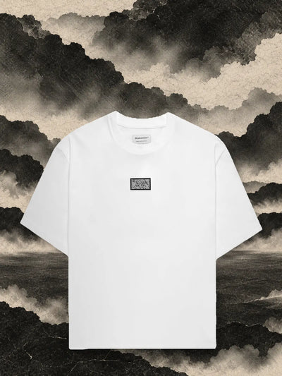 Den vita t-shirten Triodrome bland paneler av mörkt papper, under en himmel av rök av grått papper.