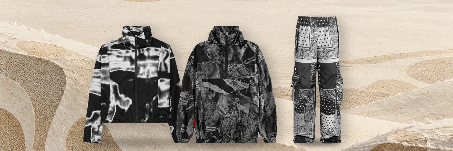 La giacca a vento Rift, l'anorak Insectide Vision e il cargo Romanticbandana in fila sulle dune di carta avorio.