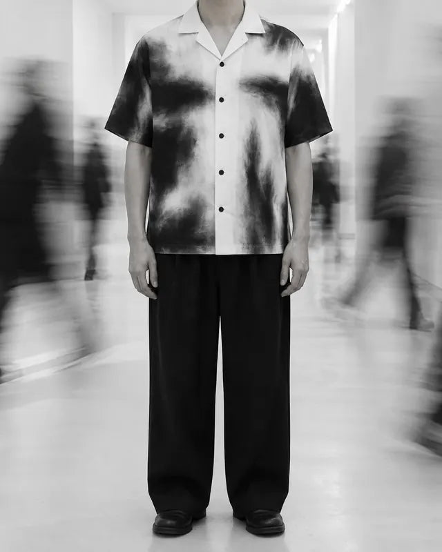 Una persona inventata, tagliata al collo, in un corridoio bianco con una camicia a macchie nere.