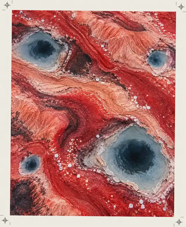Terra rossa lucida vista dall'alto, con pozze azzurre dal centro scuro e perle di sale.